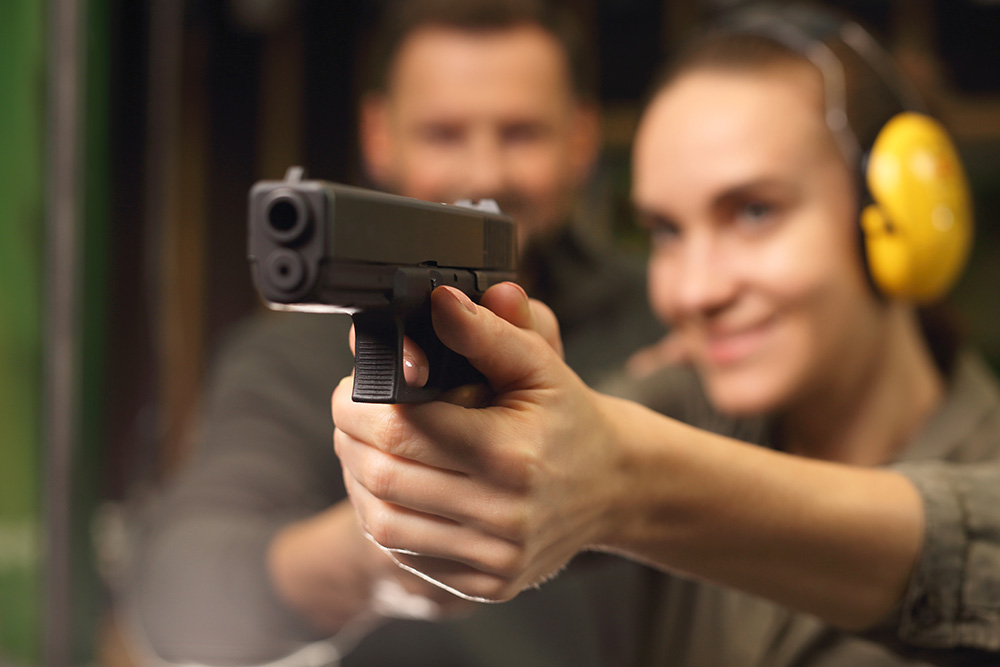 two people out of focus, shooting a black handgun in focus