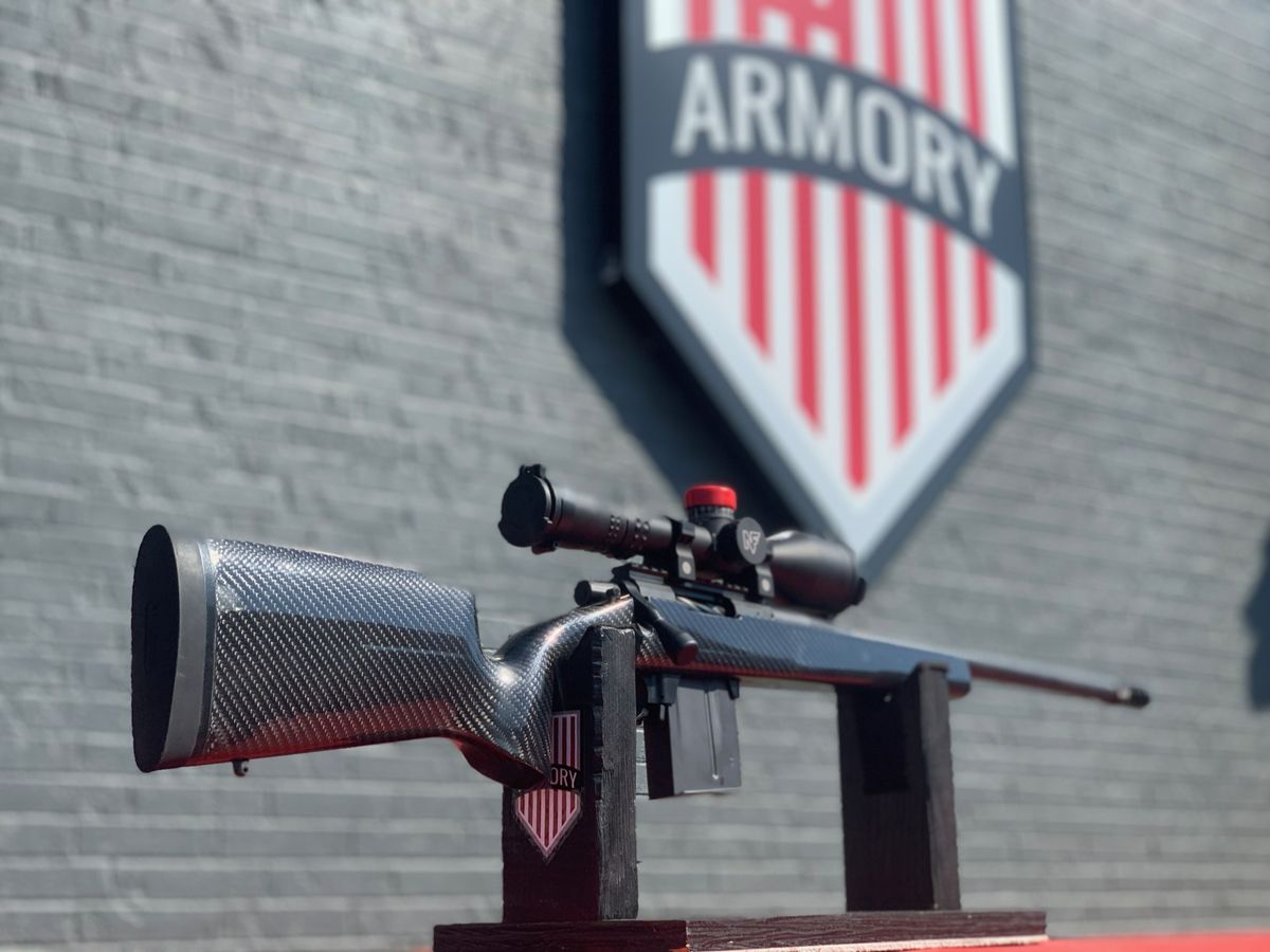 Custom rifle on a red bench in front of the 717 Armory sign
